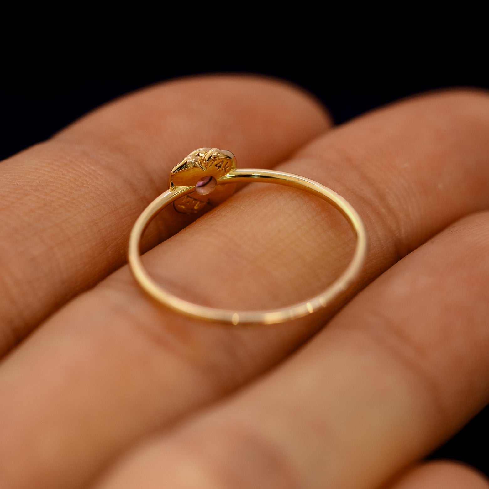 An angled view of a Pink Sapphire Gemstone Flower Ring resting on a model's fingers to show underneath the setting