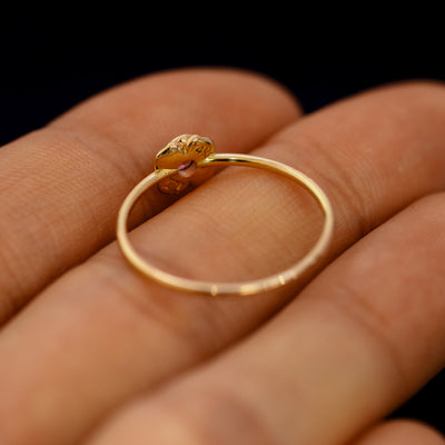 An angled view of a Pink Sapphire Gemstone Flower Ring resting on a model's fingers to show underneath the setting