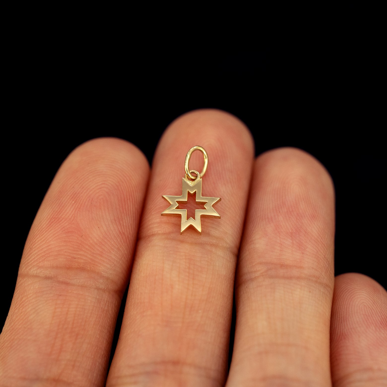 A solid gold Large Open 8 Pointed Star Charm resting in a model's hand