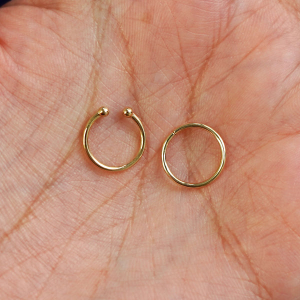 Two 14k solid gold Line Septum rings show in options of Non-Pierced and Pierced resting in the palm of a model's hand