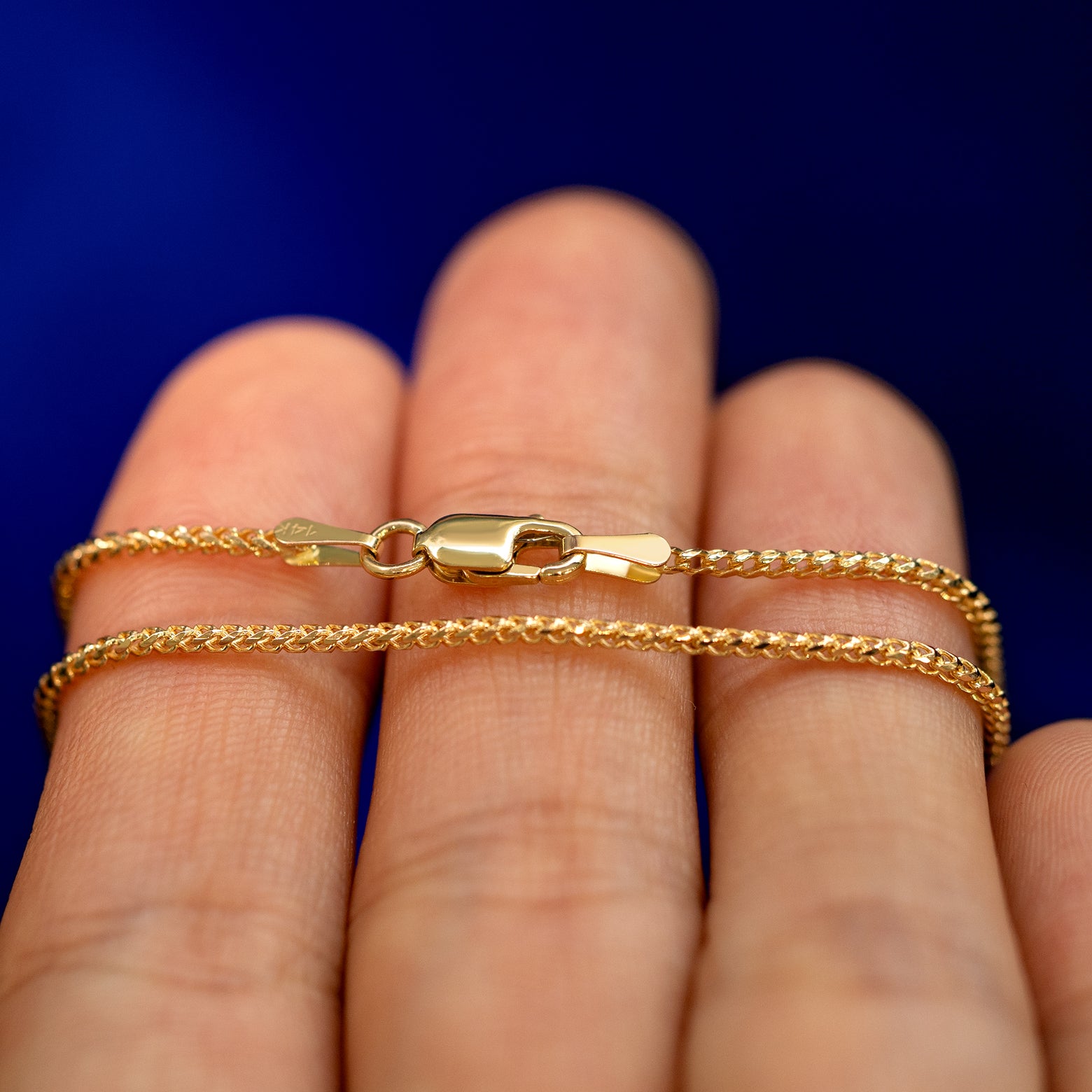 A yellow gold Mini Franco Chain Anklet wrapped around a model's fingers to show the chain and the lobster claw clasp