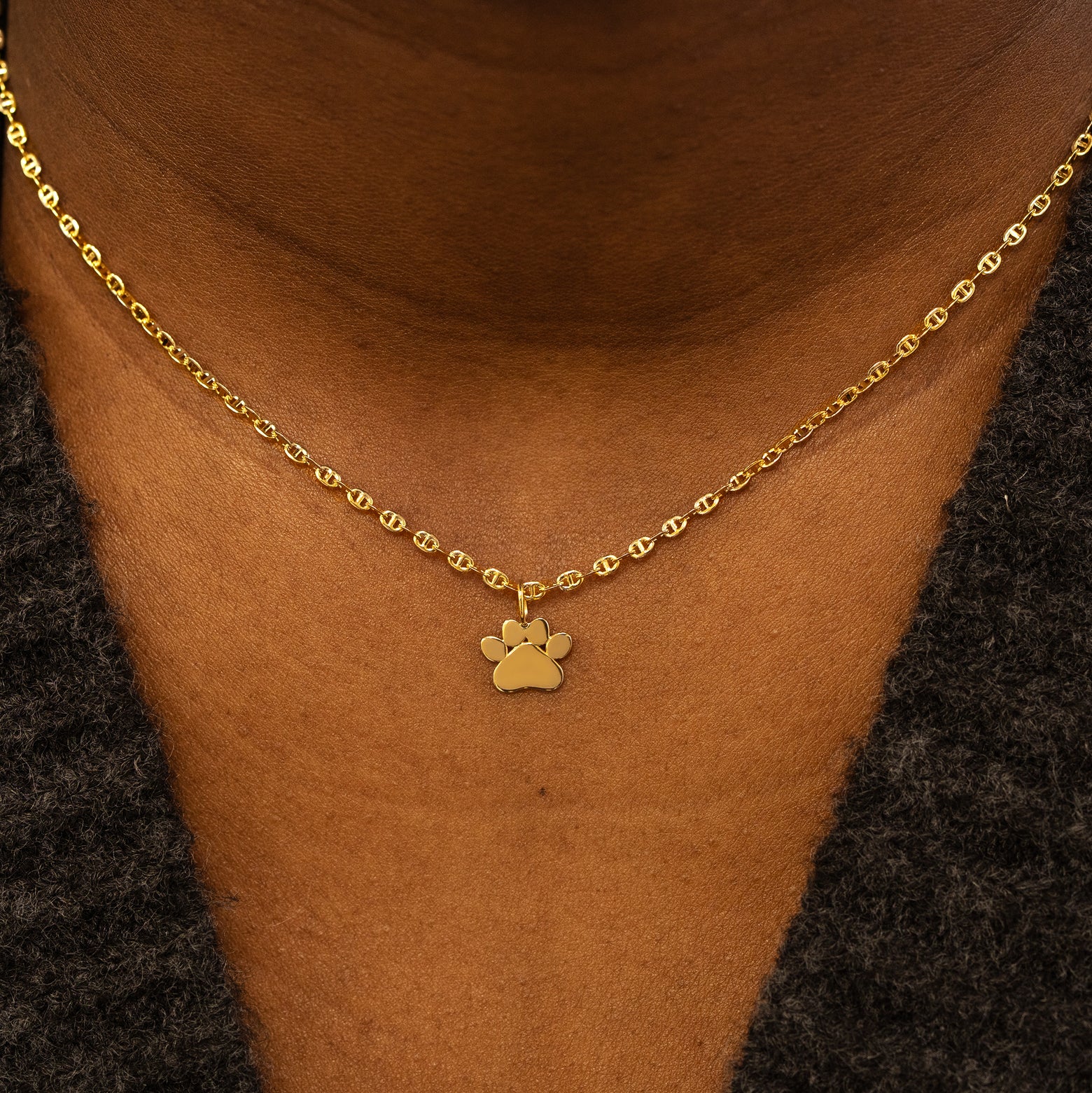 A model wearing a solid gold paw charm on a mariner chain