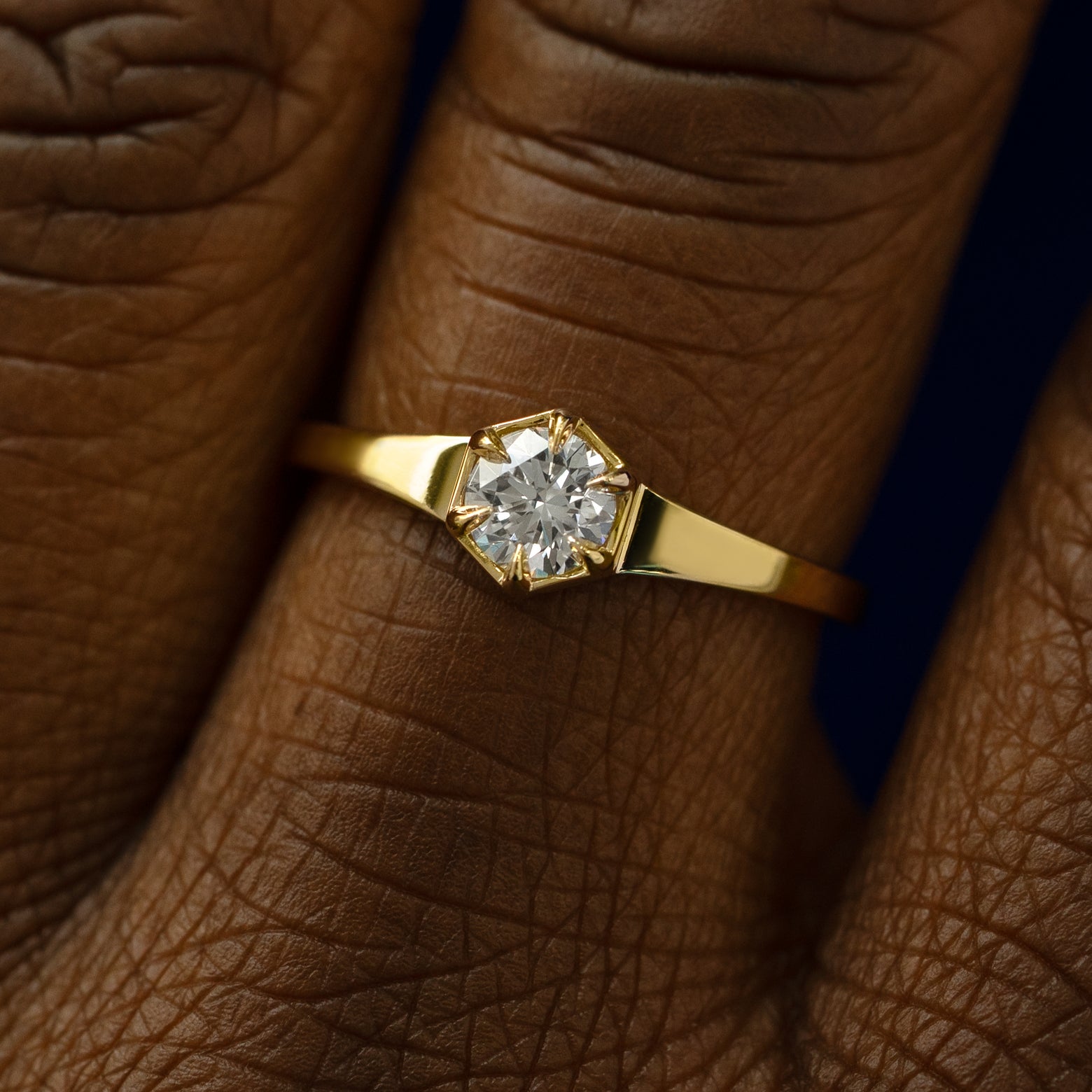 Close up view of a models fingers wearing a solid gold round diamond hexagon signet ring