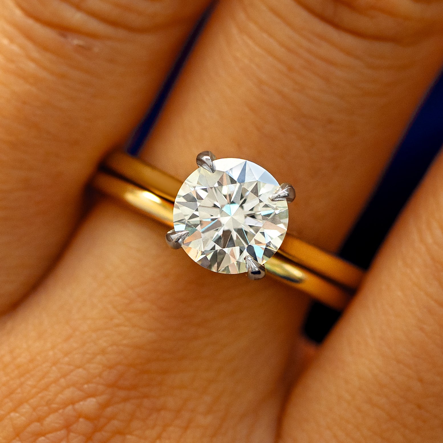 A model's fingers wearing a 14k yellow gold and platinum Round Lab Diamond Cathedral Set Ring with Curvy Mirror Band
