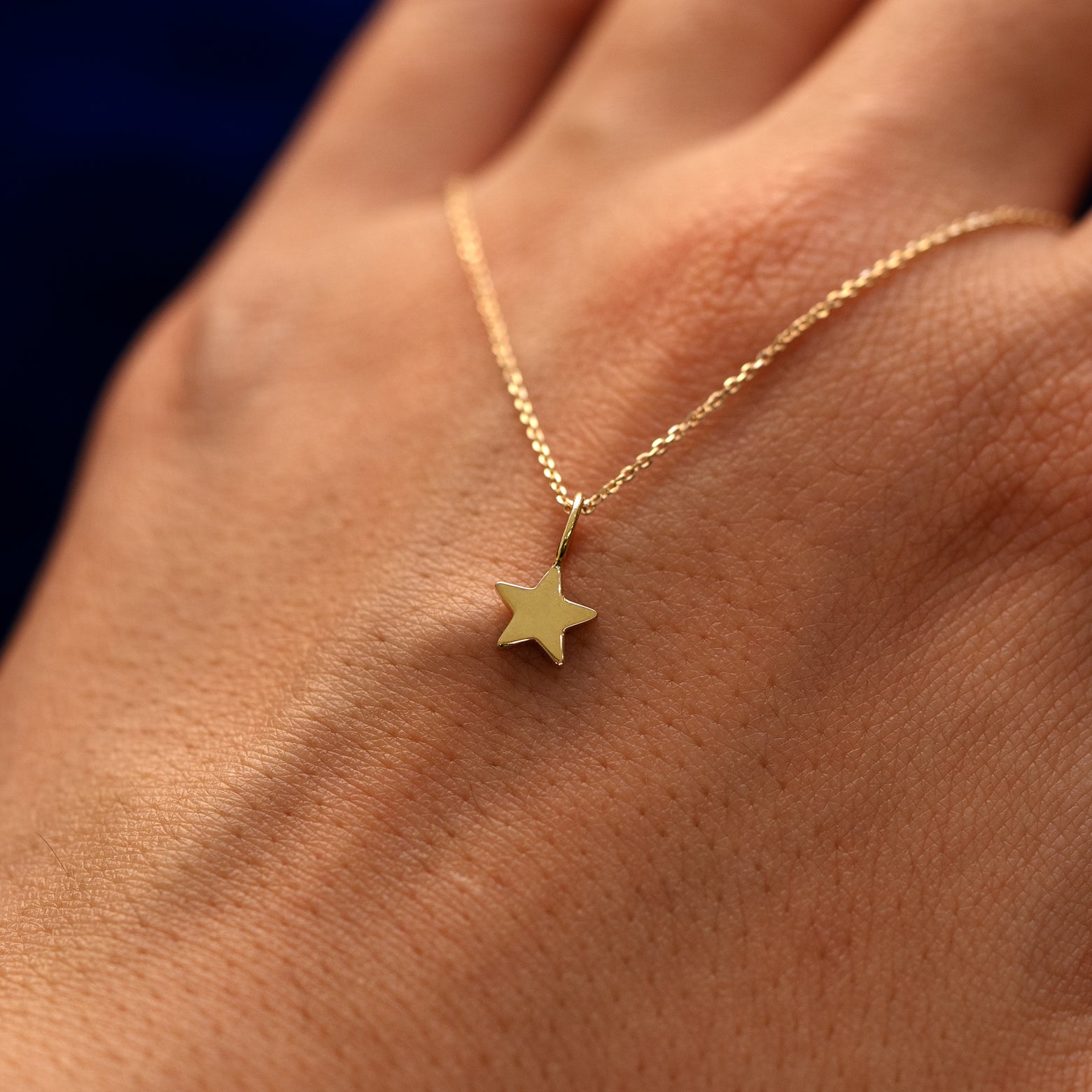 A solid 14k gold star charm on a cable chain draped over the back of a models hand