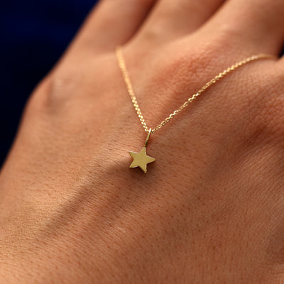 A solid 14k gold star charm on a cable chain draped over the back of a models hand
