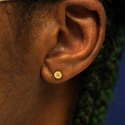 A models ear wearing a yellow gold disk earring with an engraved star on the front