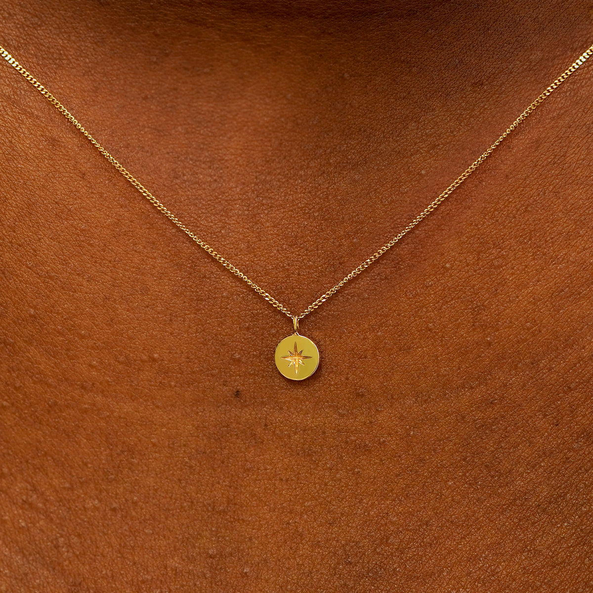 Close up view of an engraved yellow gold star disk pendant necklace on a models neck