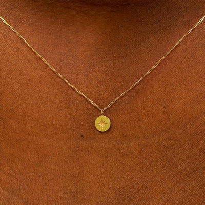 Close up view of an engraved yellow gold star disk pendant necklace on a models neck