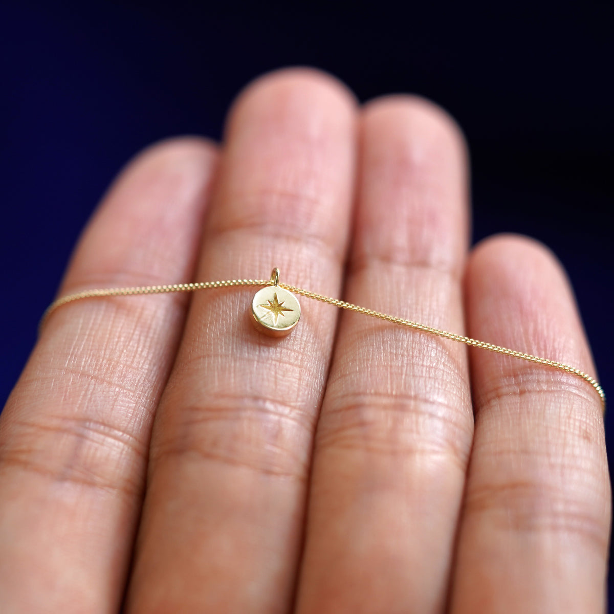 A solid yellow gold star disk necklace wrapped around the a models fingertips