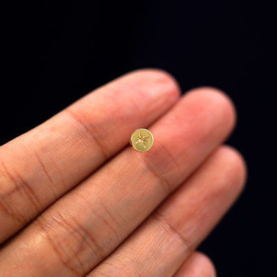 A model holding a flat circle earring with an engraved star on it in between their fingers