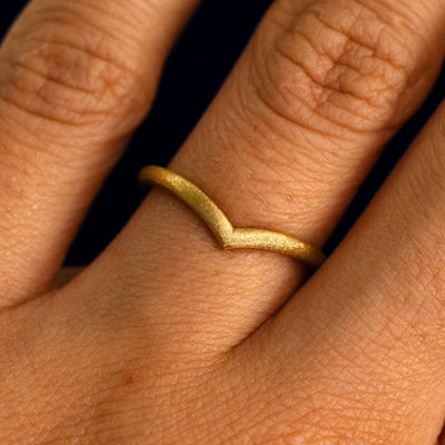 Close up view of a model's fingers wearing a 14k yellow gold stardust finish Chevron Band