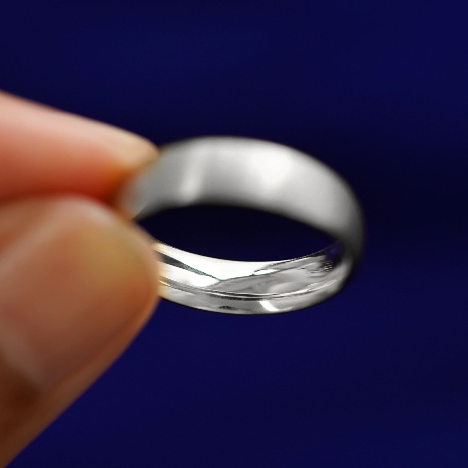 A model holding a Silver Curvy Matte Band tilted to show the inside of the band