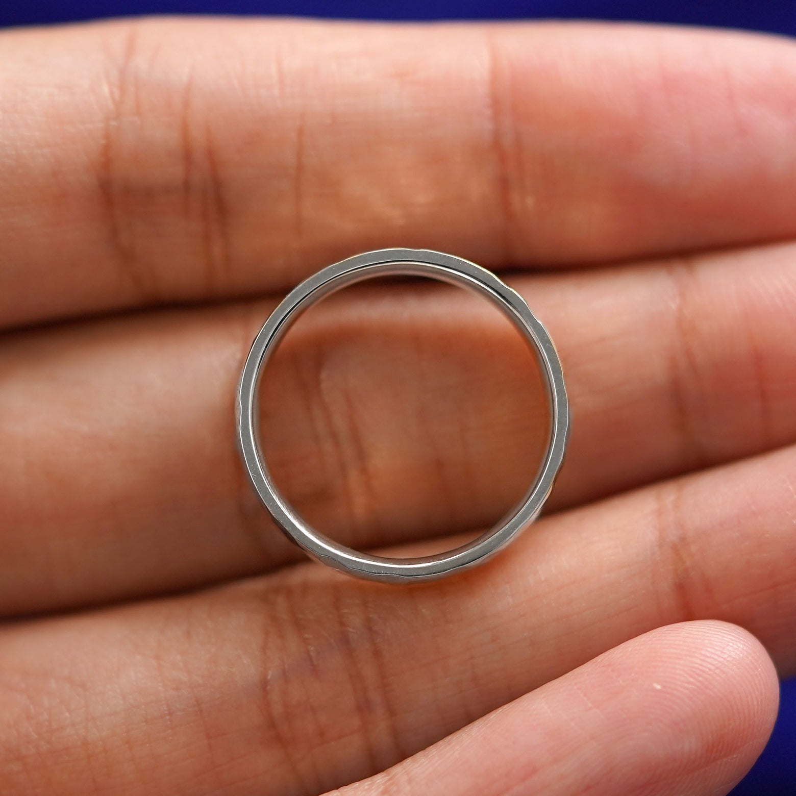 A silver Industrial Hammered Band resting on a model's fingers to show the thickness of the band