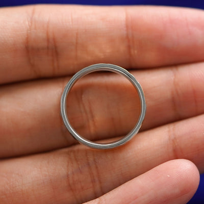 A silver Industrial Hammered Band resting on a model's fingers to show the thickness of the band
