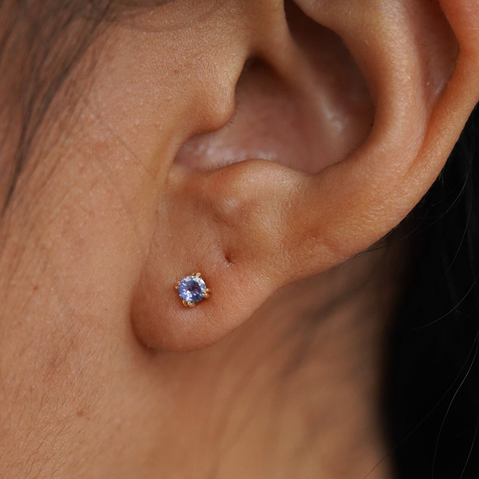 Close up view of a model's ear wearing a 14k yellow gold Tanzanite Earring