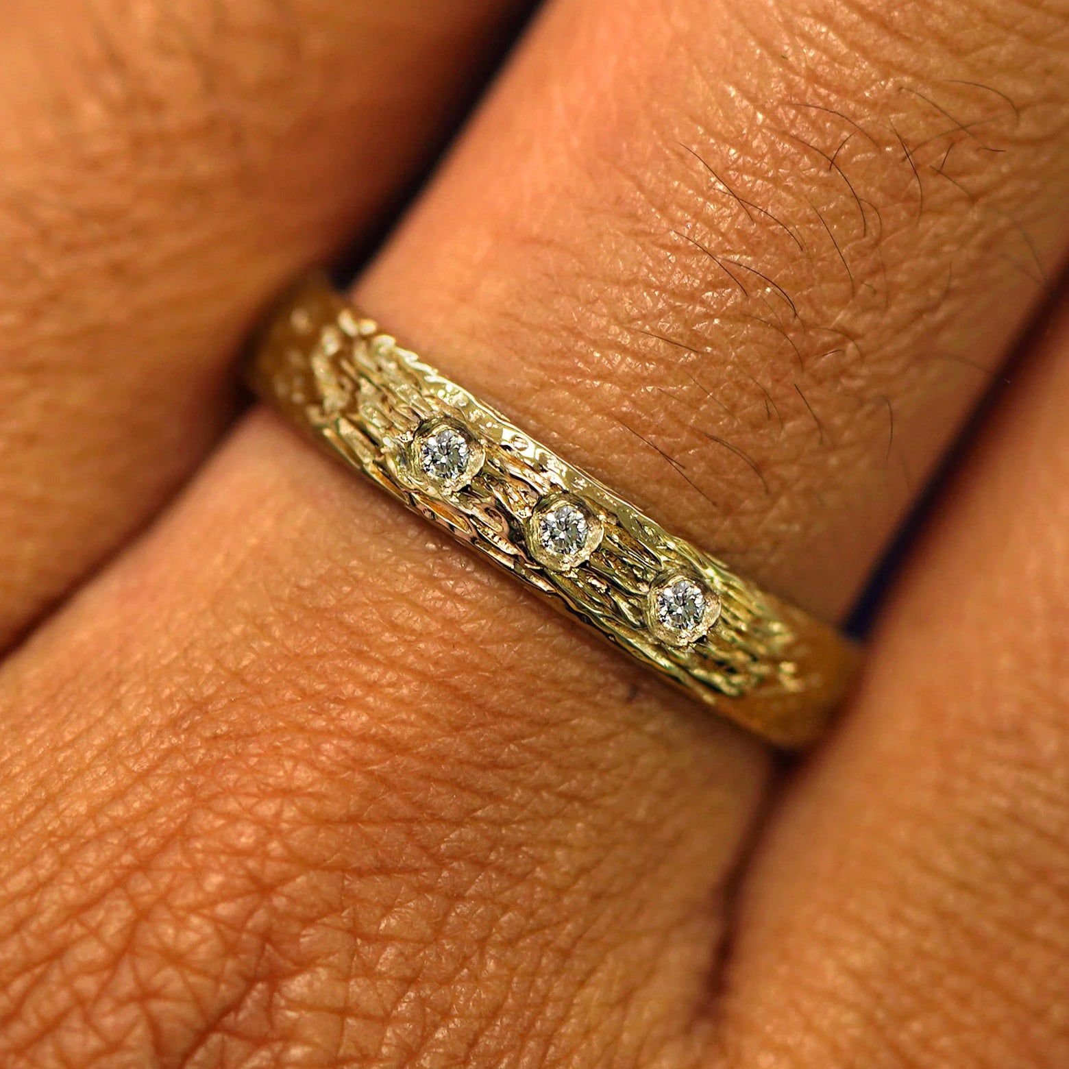 Close up view of a model's hand wearing a solid yellow gold Raw Band with one diamond