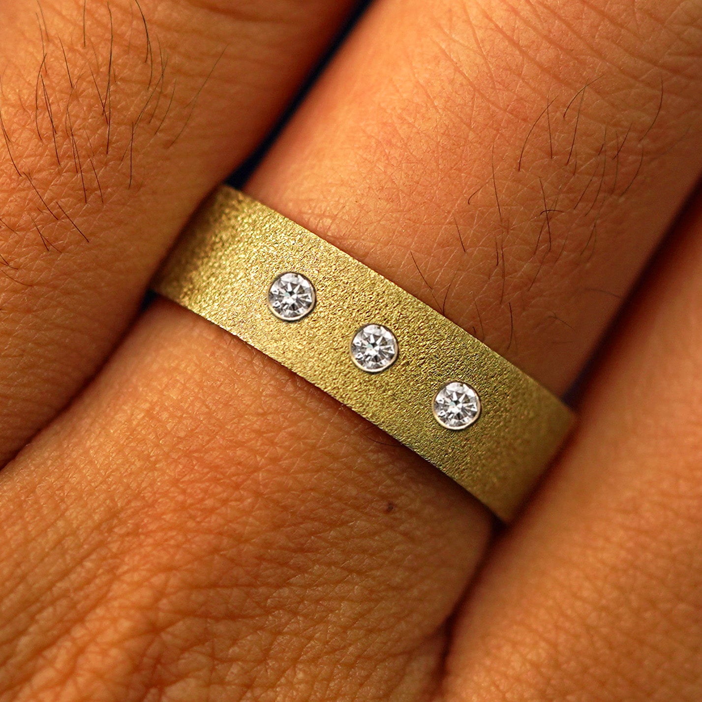 Close up view of a model's fingers wearing a 14k yellow gold Industrial Stardust Band with three diamonds