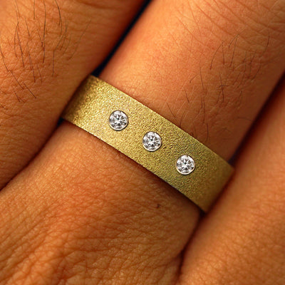 Close up view of a model's fingers wearing a 14k yellow gold Industrial Stardust Band with three diamonds