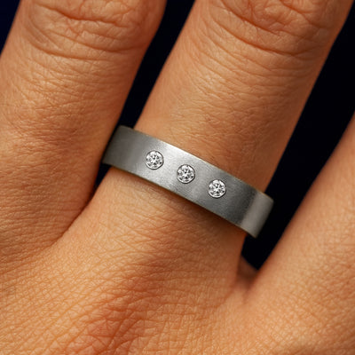 Close up view of a model's fingers wearing a platinum Industrial Matte Band with three diamonds