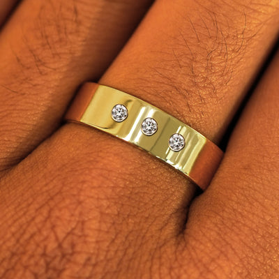 Close up view of a model's fingers wearing a 14k yellow gold Industrial Mirror Band with three diamonds