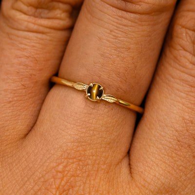 A solid 14k yellow gold Tiger Eye Gemstone Two Leaf Ring on a model's finger