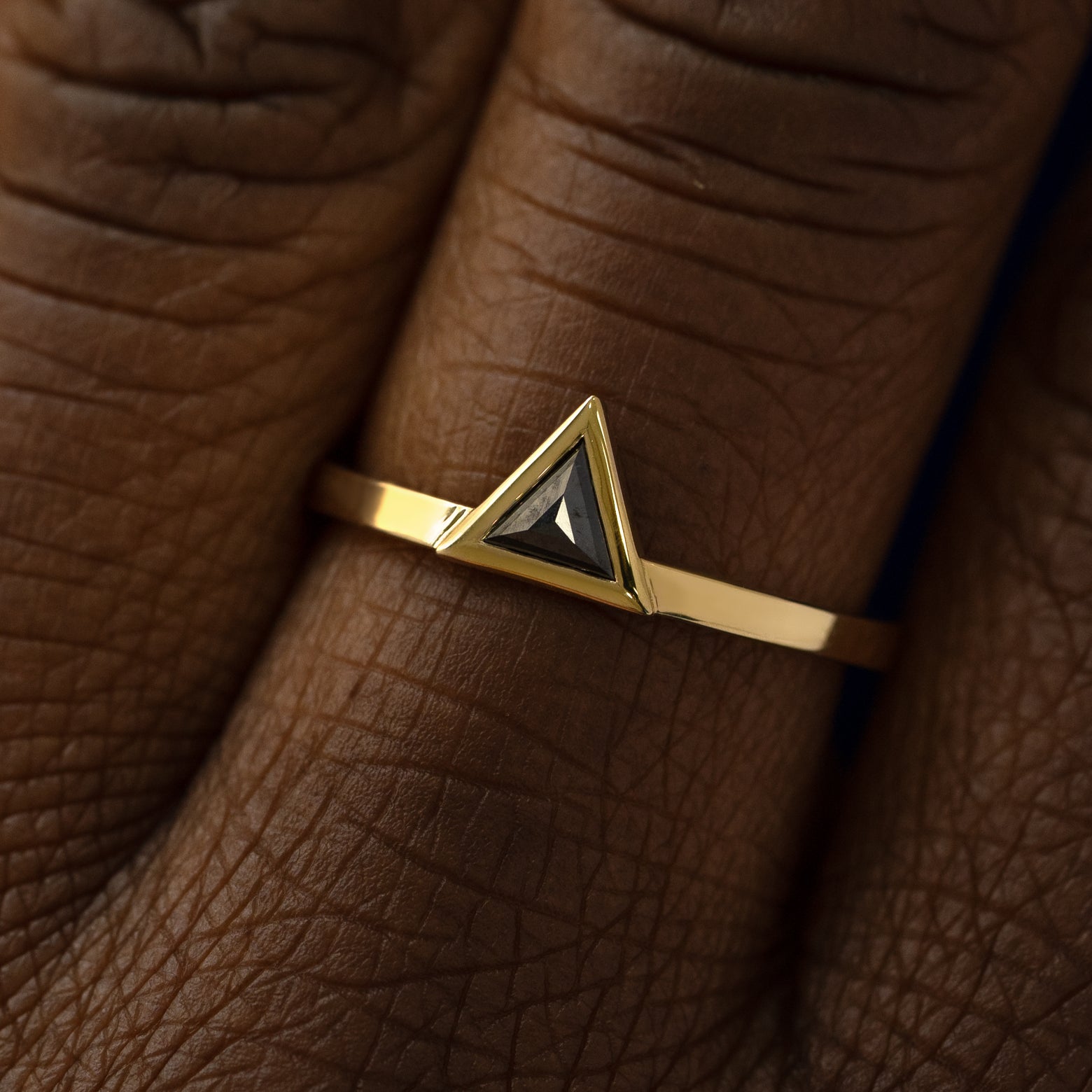 Close up view of a model's hand wearing a 14k yellow gold Triangle Black Diamond Ring