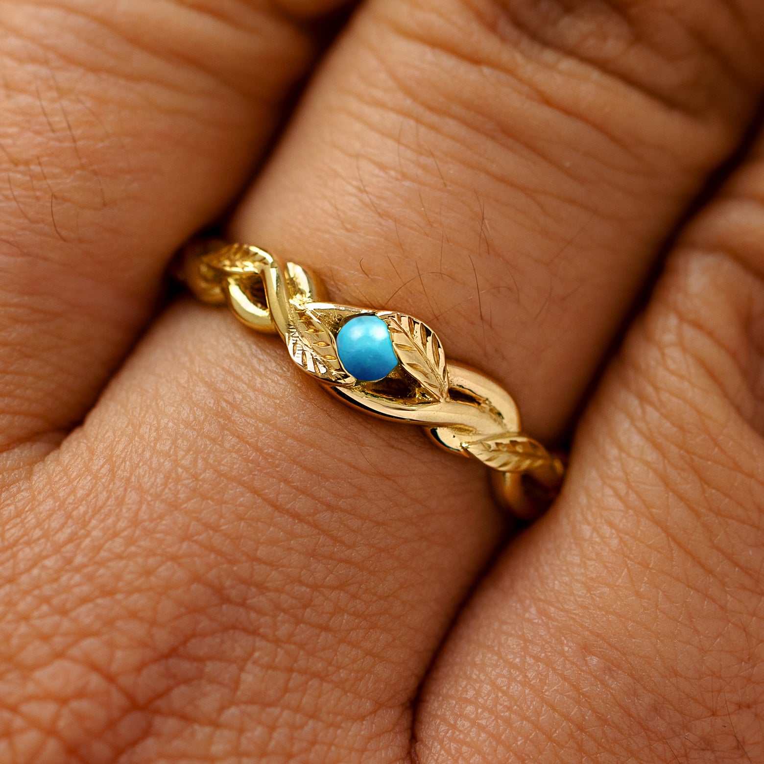 A solid 14k yellow gold turquoise leaves and vines ring on a model's finger