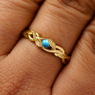 A solid 14k yellow gold turquoise leaves and vines ring on a model's finger