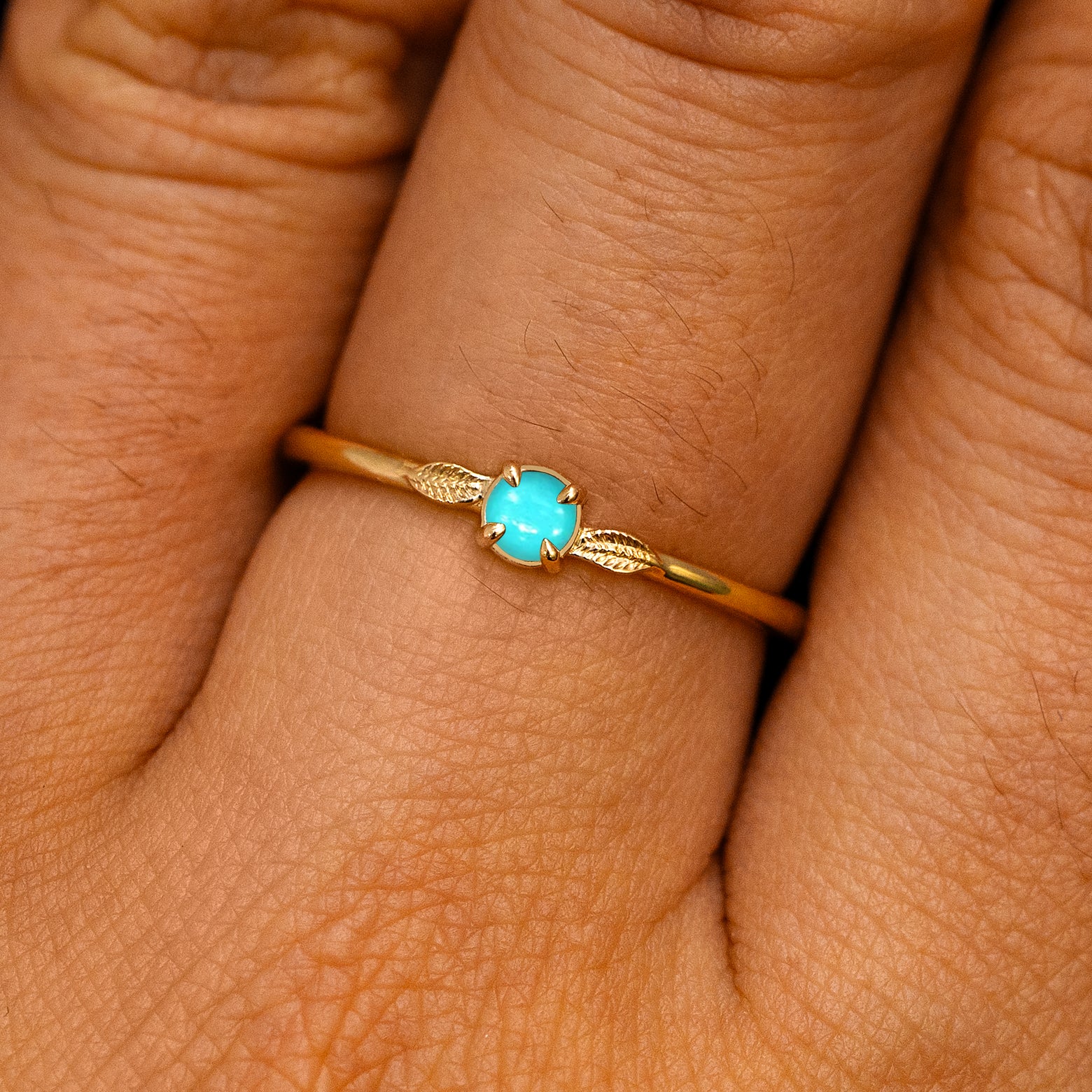 A solid 14k yellow gold Turquoise Gemstone Two Leaf Ring on a model's finger