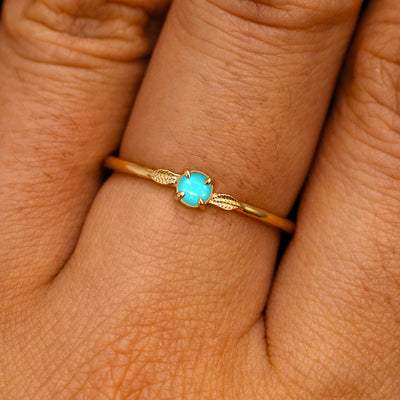 A solid 14k yellow gold Turquoise Gemstone Two Leaf Ring on a model's finger