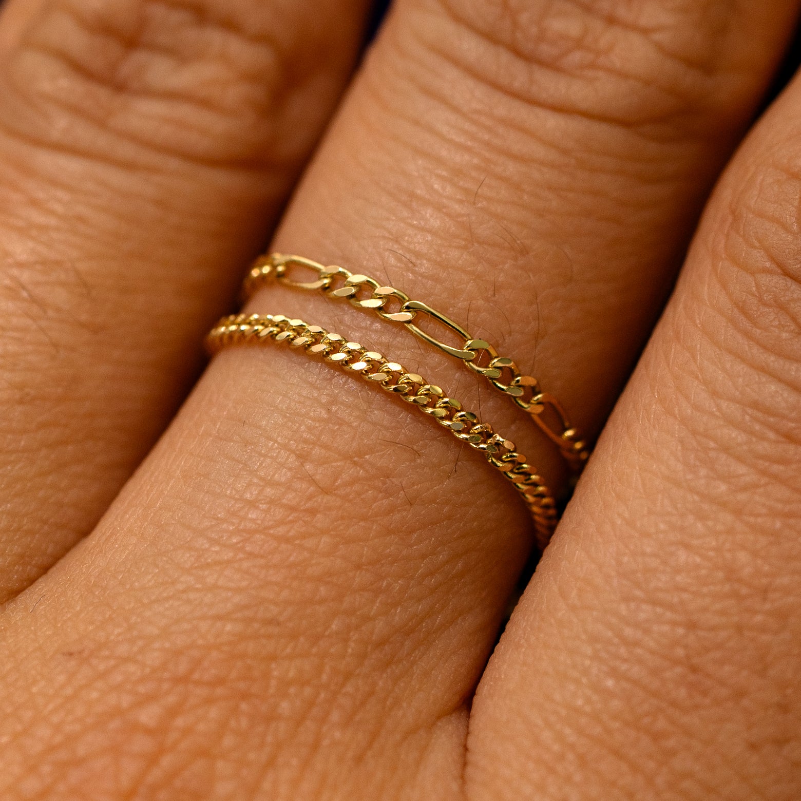 Close up view of a model's finger wearing a mini Miami chain ring and a figaro chain ring stacked