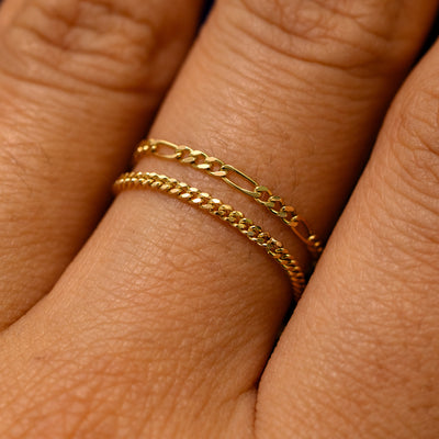 Close up view of a model's finger wearing a mini Miami chain ring and a figaro chain ring stacked