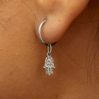 Close up view of a model's ear wearing a white gold Hamsa hand charm on a Small Seamless Huggie Hoop