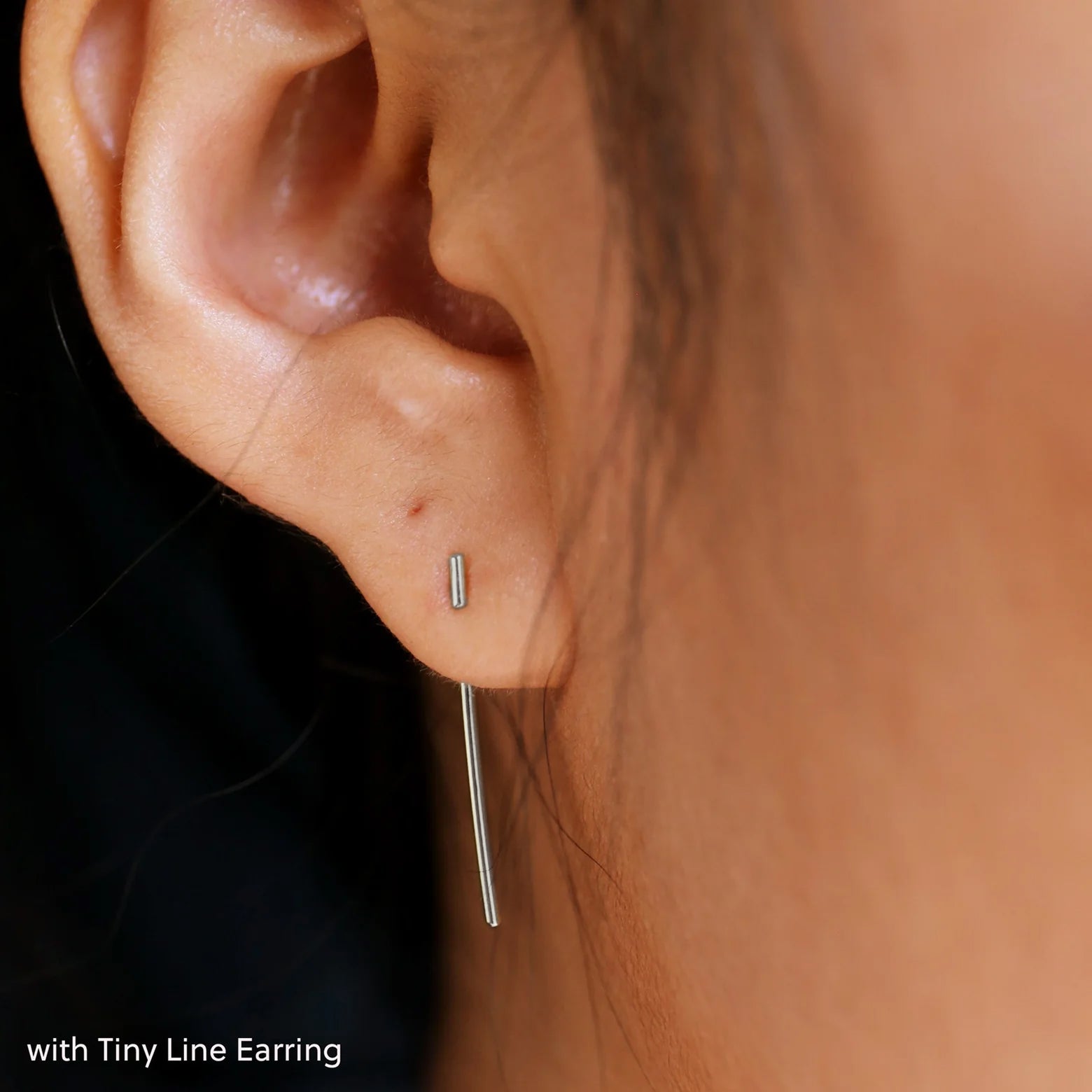 Close up view of a model's ear wearing a white gold Line Jacket with a Tiny Line Earring