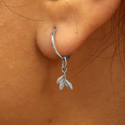 Close up view of a model's ear wearing a white gold 3 Leaves Charm on a Small Seamless Huggie Hoop
