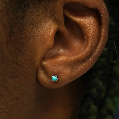 Close up view of a model's ear wearing a 14k white gold turquoise 3mm Gemstone Earring