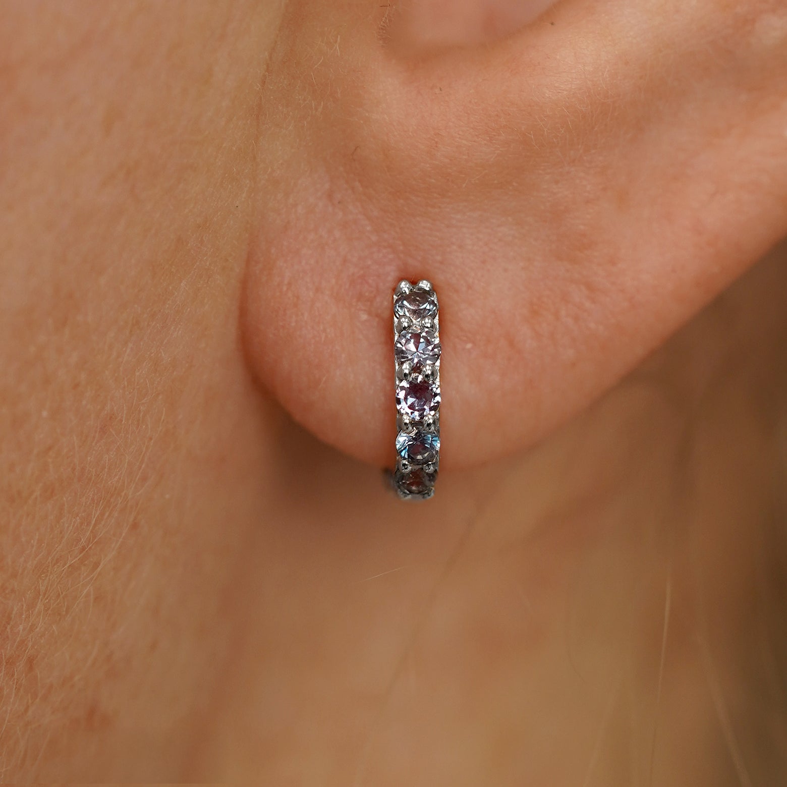 Close up view of a model's ear wearing a white gold Mini Alexandrite Huggie Hoop