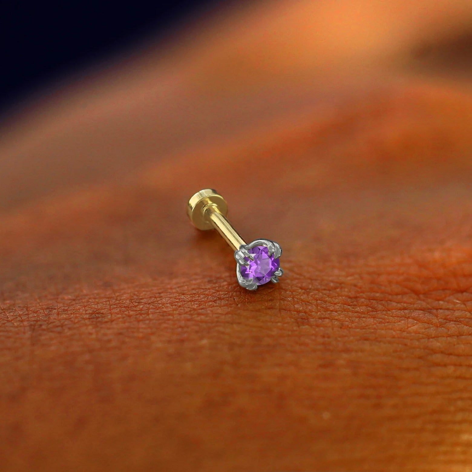 A solid 14k white gold Amethyst Flatback Piercing resting on the back of a model's hand