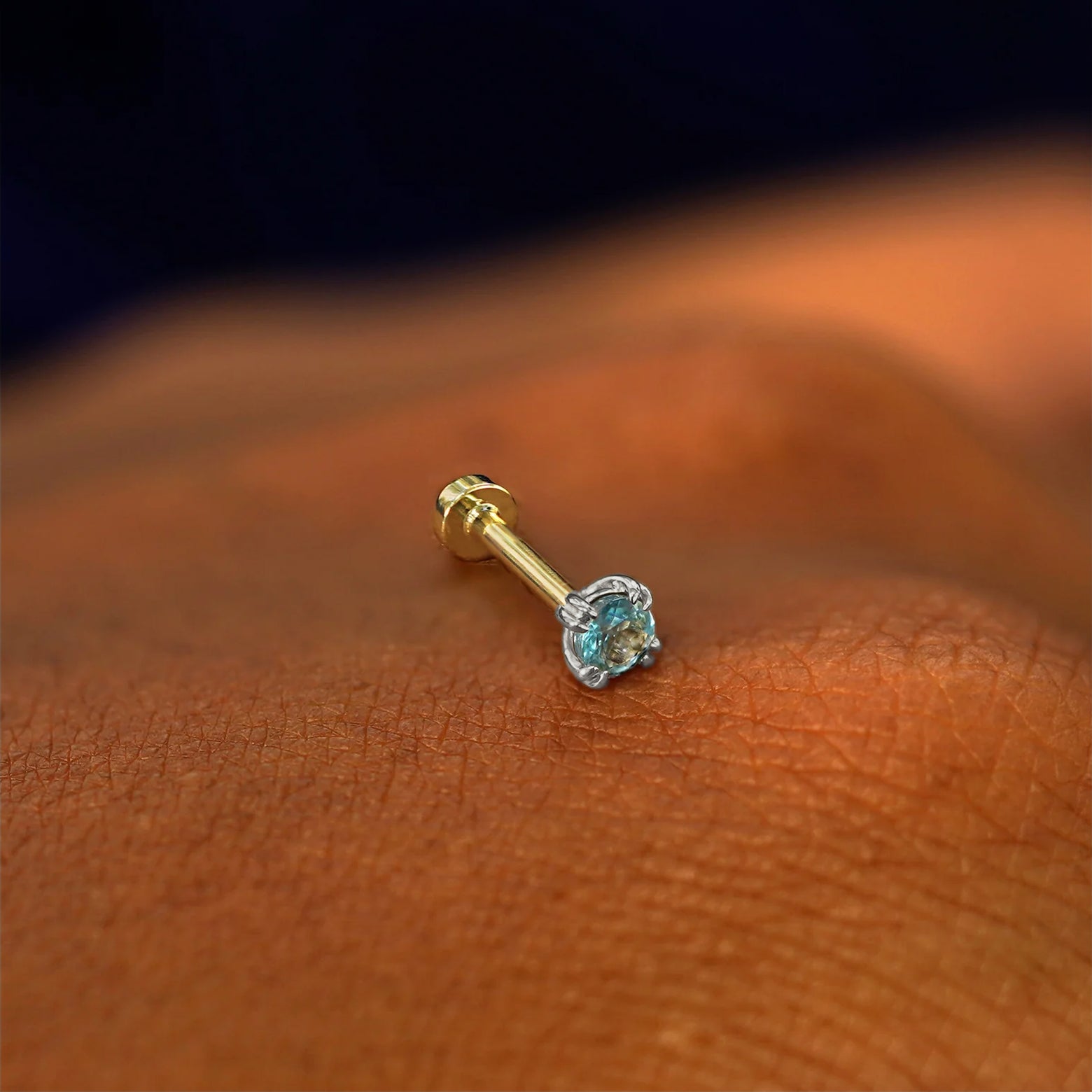 A solid 14k white gold Aquamarine Flatback Piercing resting on the back of a model's hand