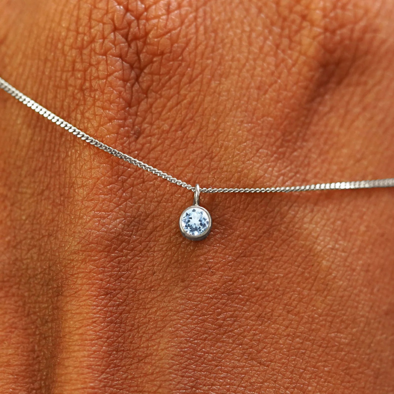 Close up view of a 14k white gold Aquamarine Necklace draped across the back of a model's hand