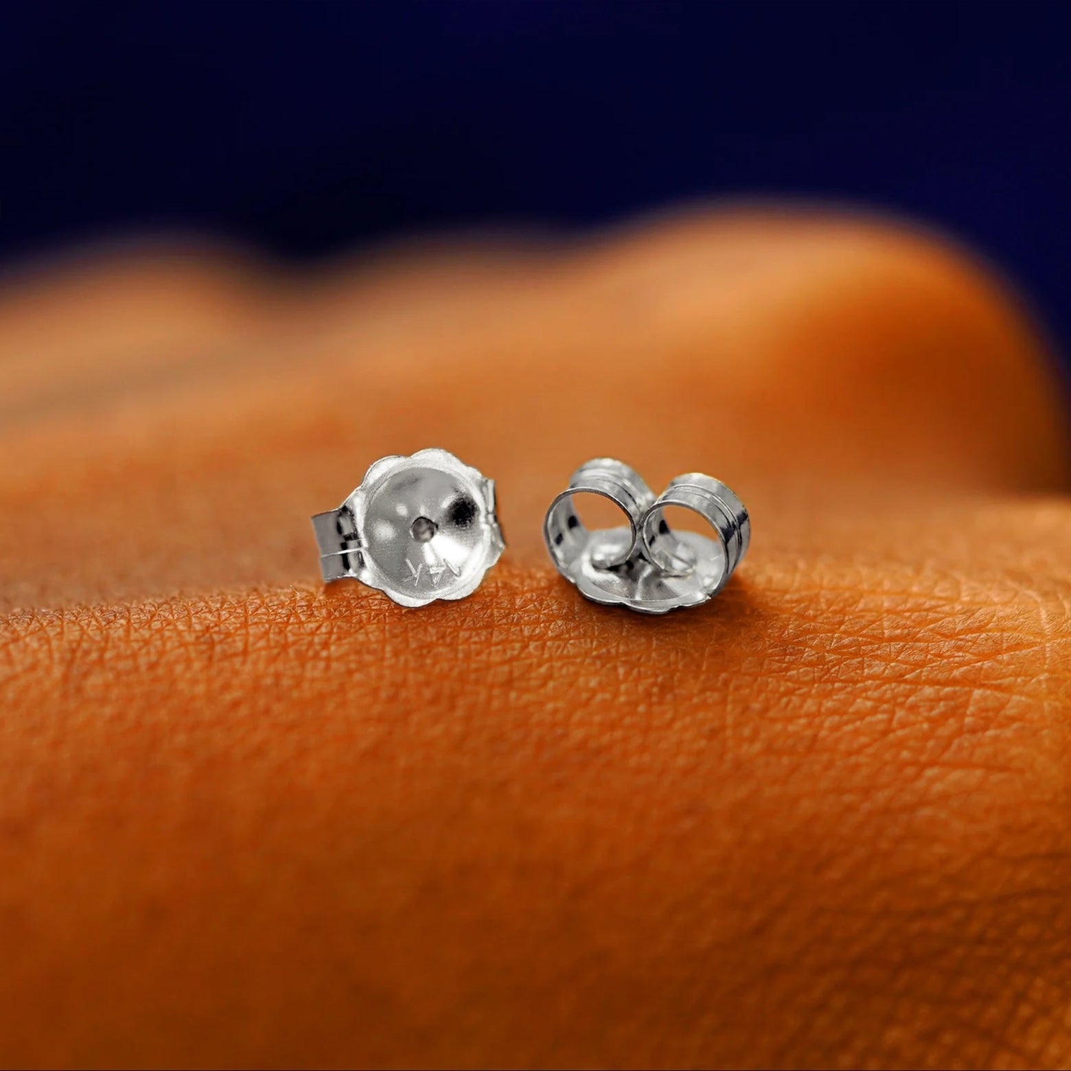 A pair of solid white 14k gold large push back earring backings on the back of a hand