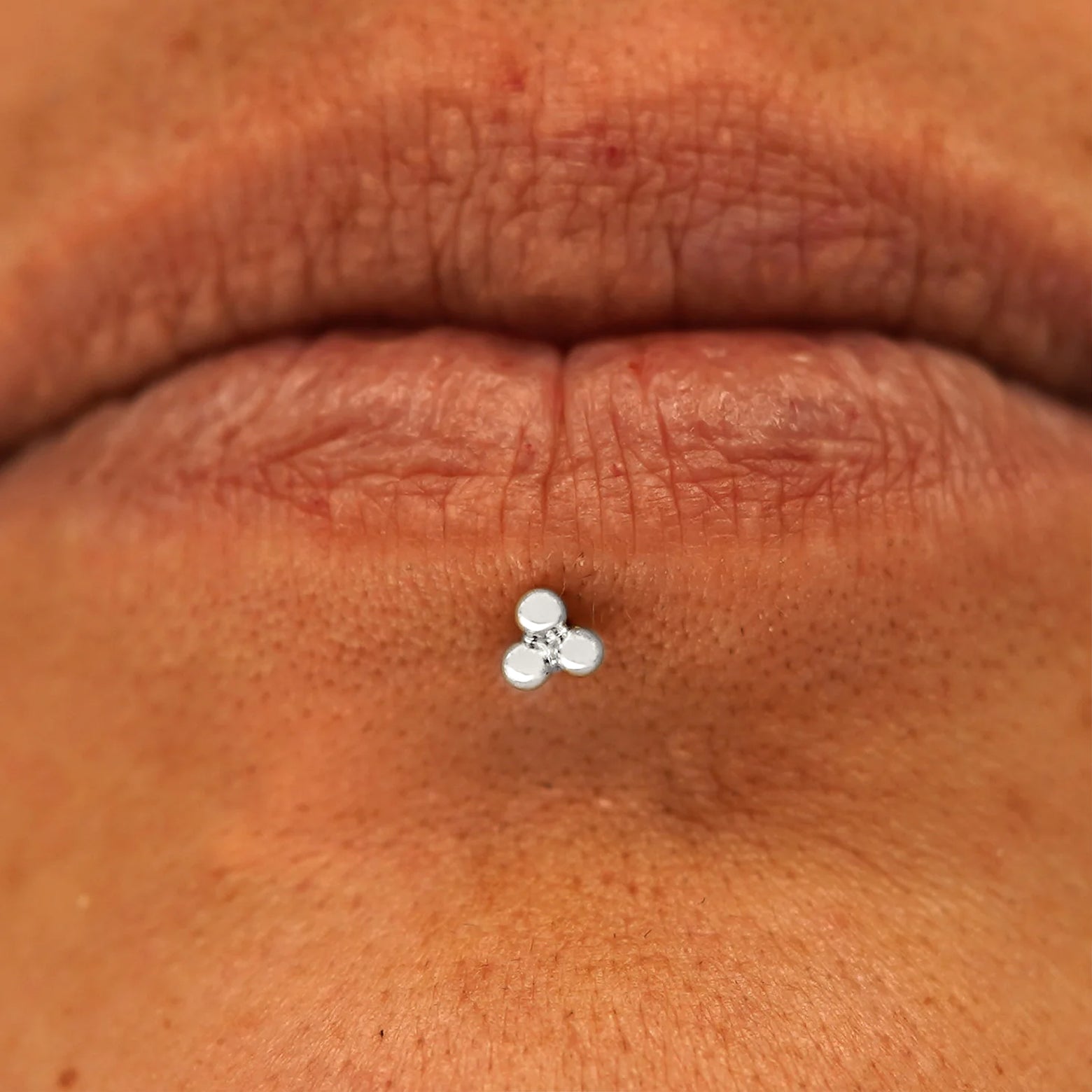 Close up view of a model's mouth wearing a 14k white gold Ball Trio Flatback as a labret piercing