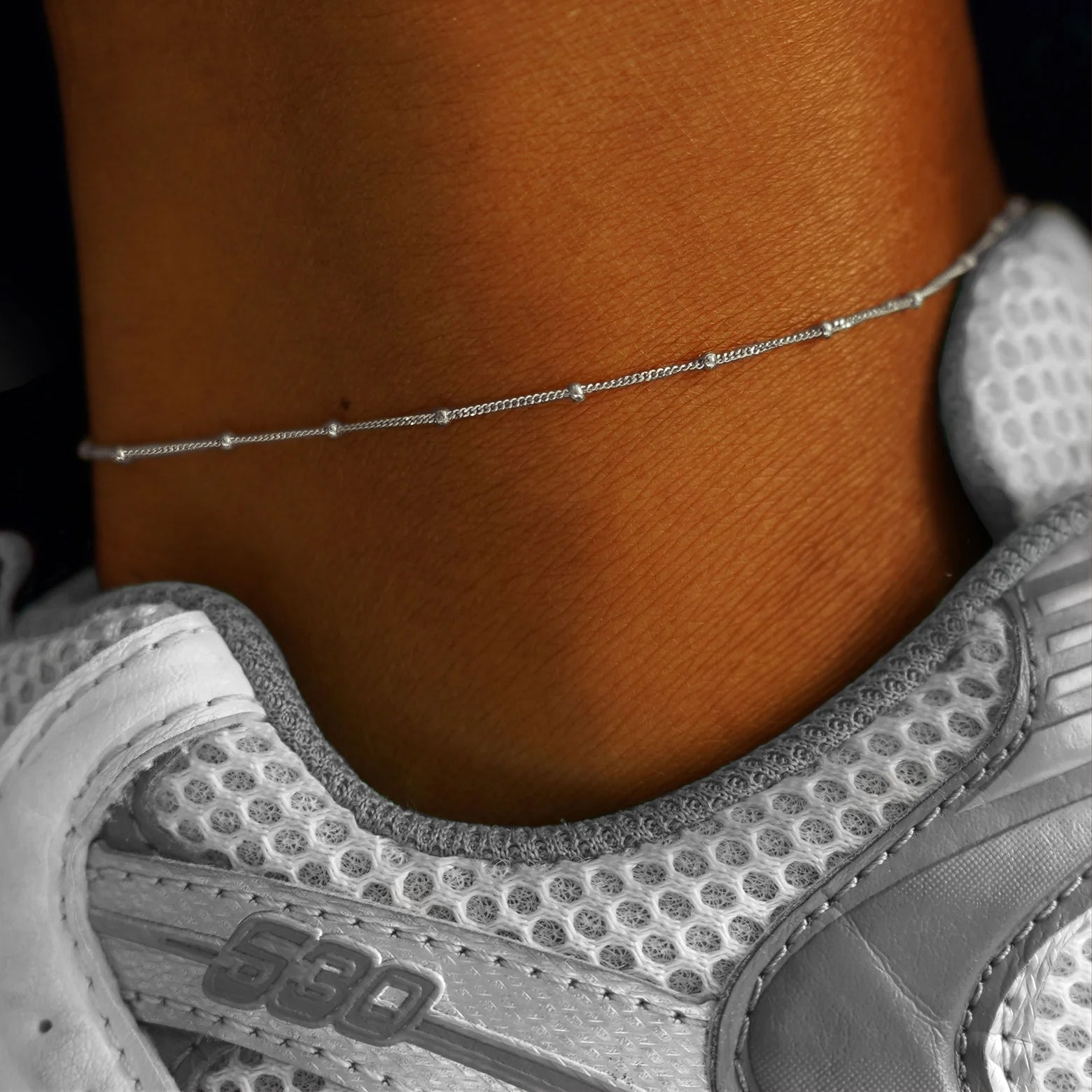 Close up view of a model's ankle wearing a white gold Beads Anklet