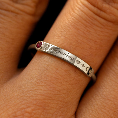 A model's finger wearing a ruby white gold bezel set gemstone bar ring with the word engraving in cursive font