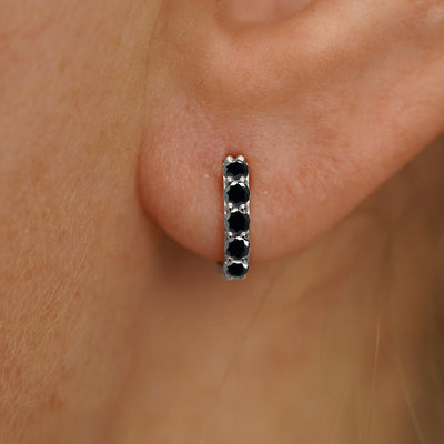 Close up view of a model's ear wearing a white gold Mini Black Diamond Huggie Hoop