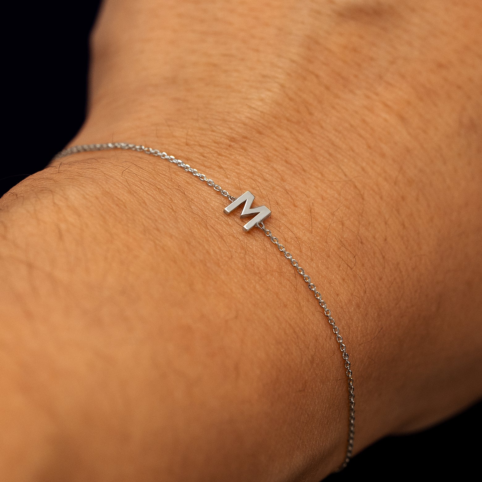 Close up view of a model's wrist wearing a 14k white gold block initial bracelet with the letter M