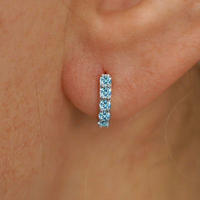 Close up view of a model's ear wearing a white gold Mini Light Blue Lab Diamond Huggie Hoop