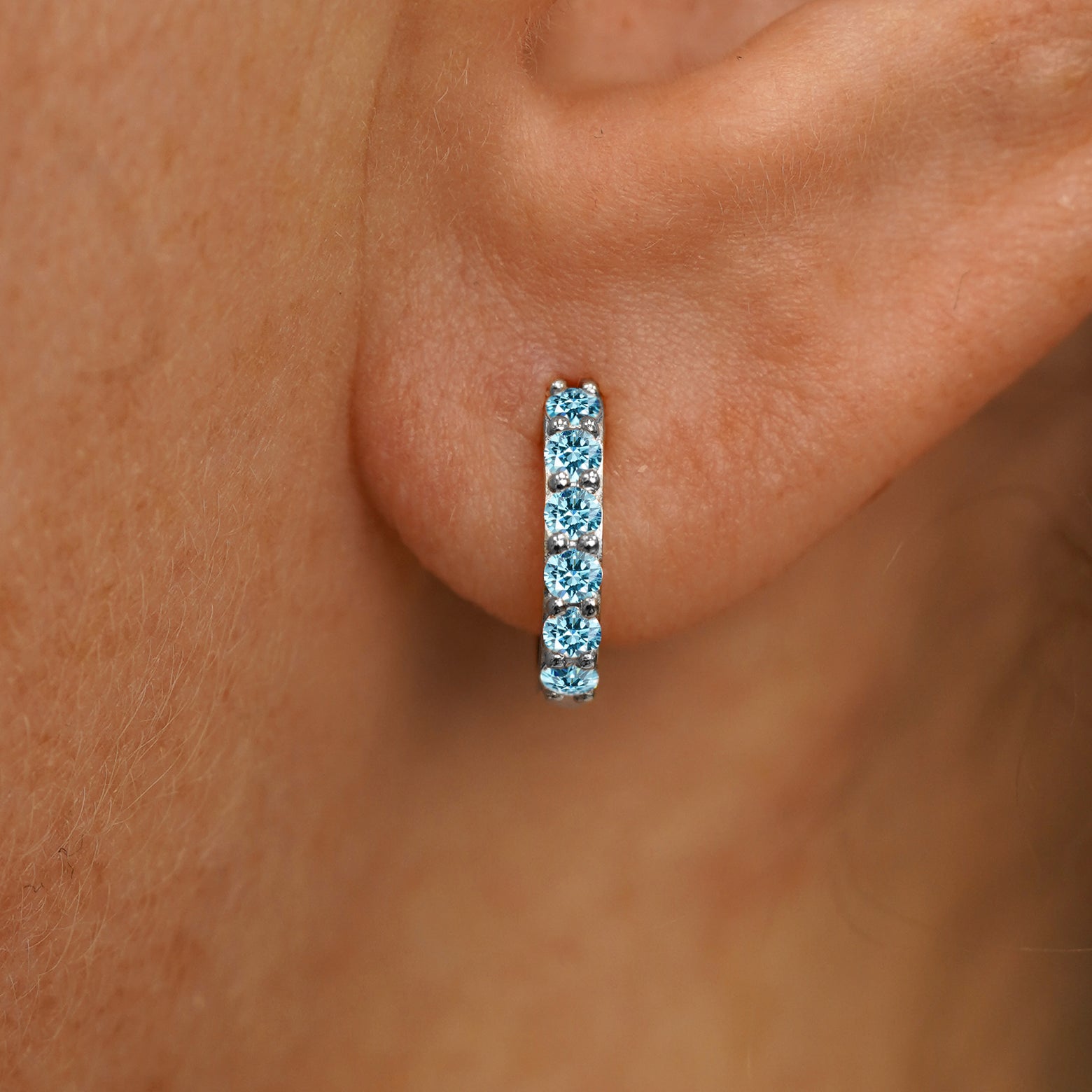 Close up view of a model's ear wearing a white gold Small Light Blue Lab Diamond Huggie Hoop