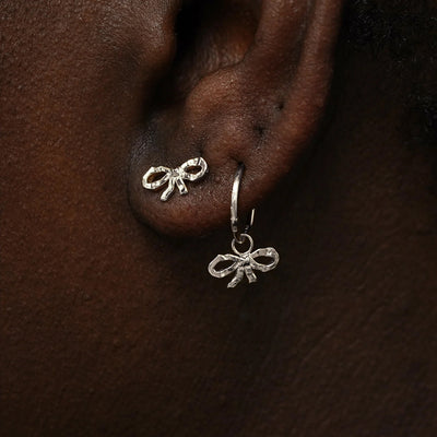 A model wearing a Bow Earring and a white gold Bow Charm on a rope huggie hoop